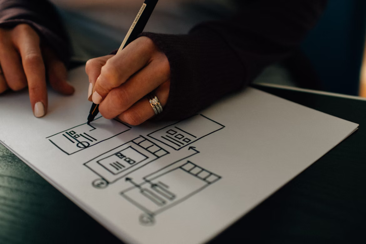 Close-up of a person sketching a flowchart or design layout on paper with a pen.